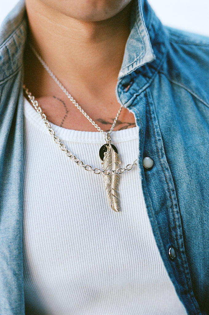 O.P Jewellery recycled 925 silver SKATA SKATA Big Feather Pendant worn on a person with a white ribbed t-shirt and denim shirt.
